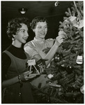 Two women hang KUHT ornaments on a Christmas tree