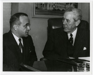 Two men talk at desk