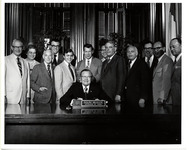Dolph Briscoe sitting at his desk with a group of people behind him