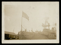 USS Houston (CA-30) docked with crew on deck and American flag flying from bow