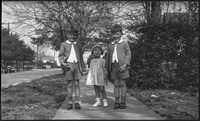 Group photograph of two boys and a young girl standing on a sidewalk