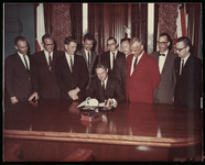 John Bowden Connally signing a paper with a group of men watching on
