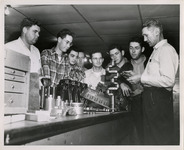 Professor and a group of students standing around a disassembled engine on a work bench