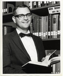 Edward G. Holley in front of stacks with a book