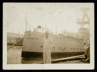 USS Houston (CA-30) docked with crew member standing on dock in front of bow